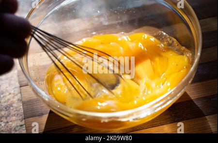 Whipping eggs in a glass bowl. Egg yolks and egg whites mixed with spices. Stock Photo