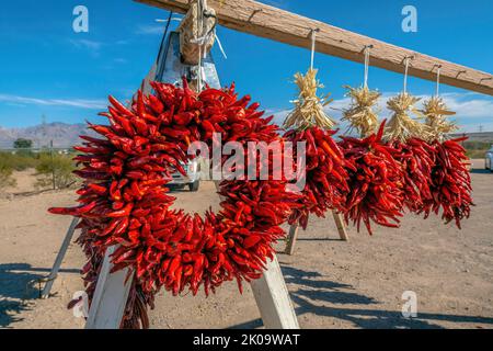 Hanging wreath of red chili peppers for sale on the side of the road at Tucson, Arizona. Wreaths of bright red chili peppers against the view of mount Stock Photo