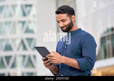 Smiling indian professional business man using digital tablet outdoors. Stock Photo