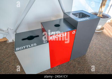 View of three trash bins with bottles, cans, and waste signs- Tucson, Arizona. There is a white bin on the left for bottles, red recycle bin for can i Stock Photo