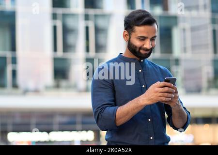 Indian business man using smartphone standing in urban city street outdoors. Stock Photo