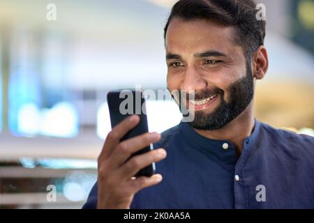 Smiling indian business man using smartphone looking at cellphone. Stock Photo