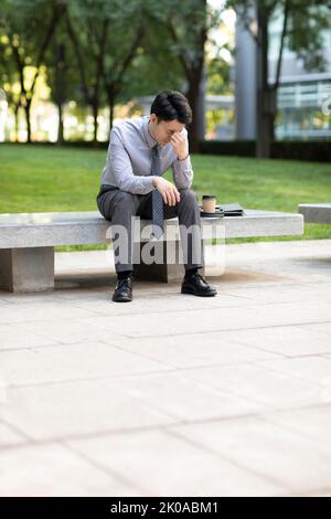 Tired young Chinese businessman sitting outdoors Stock Photo