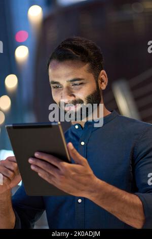 Indian business man using digital tablet outdoors in night city, vertical. Stock Photo