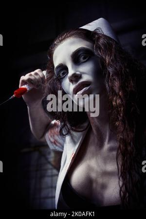 Horror shot: the ugly evil crazy nurse (doctor) in bloody uniform killing by syringe. Zombie woman (living dead). Monster from nightmare. Grunge textu Stock Photo