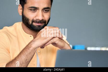 Thoughtful indian businessman looking at laptop watching business webinar. Stock Photo
