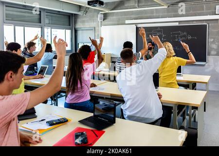 Group of high school students raising hands in classroom Stock Photo