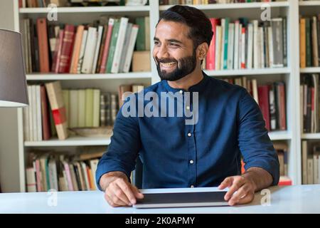 Happy smiling indian ethnic business man sitting at work desk with laptop. Stock Photo
