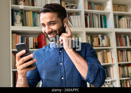 Happy indian business man wearing earbud having video call using mobile phone. Stock Photo