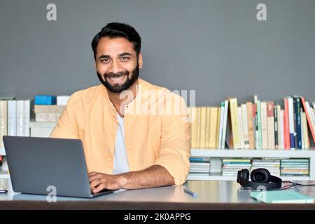 Happy indian business man working on laptop in office sitting at desk, portrait. Stock Photo