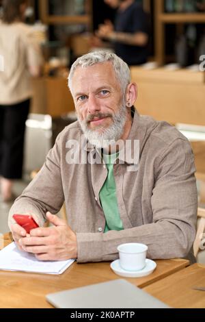 Middle aged business man using smartphone sitting at cafe table. Vertical Stock Photo