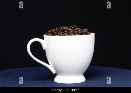 White ceramic cup filled with coffee beans against a black background Stock Photo