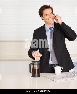 Young business man using cellphone while preparing coffee. Happy business man talking over cellphone while preparing coffee at home. Stock Photo