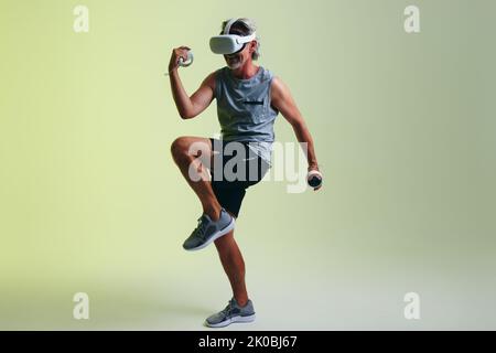 Happy senior man smiling while working out in virtual reality. Athletic senior man doing fitness exercises using pair of gaming controllers. Mature ma Stock Photo