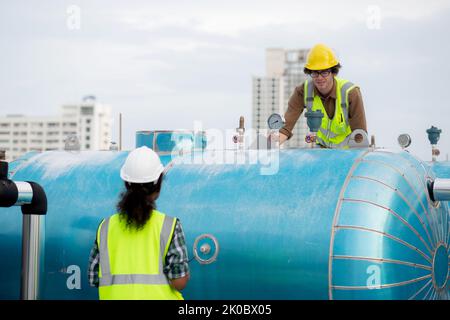 Young woman and man engineer examining pipeline and talking in the factory, mechanic or technician inspector and check plumber valve and discussion to Stock Photo