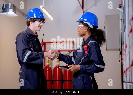 Electrical young woman and man engineer examining maintenance cabinet system electric and handshake while agreement together in control room at factor Stock Photo