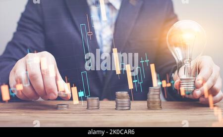 The hand puts a stack of coins with a growing business graph. Panoramic business banner with copy space. The idea arose from a burning light bulb Stock Photo