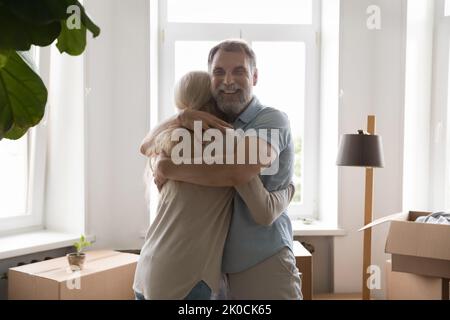 Happy retired grey haired couple hugging among moving boxes indoors Stock Photo