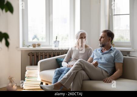 Serious concerned senior couple talking on home couch Stock Photo
