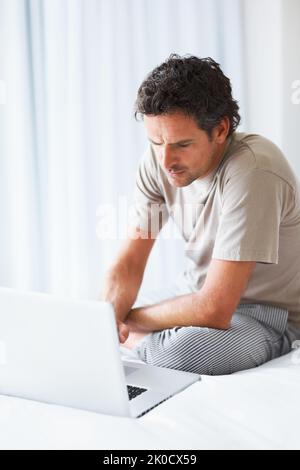 Man working on laptop. Serious mature man sitting on bed and working on laptop. Stock Photo