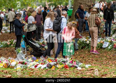 Young girl pausing to view flower tributes in Green Park following the death of Queen Elizabeth II. Child standing to read messages Stock Photo