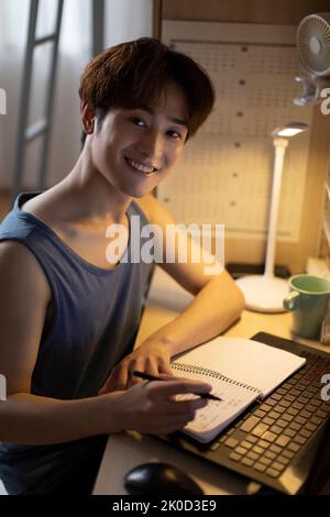 Young Chinese university student using laptop in dormitory Stock Photo