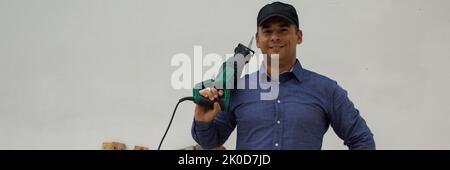 smiling handyman with a hacksaw on his shoulder while cutting and dismantling wooden pallets and platforms. Reuse of wood for do-it-yourself works. Stock Photo