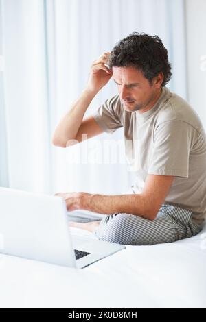Thoughtful man using laptop. Thoughtful mature man looking at laptop while sitting on bed. Stock Photo