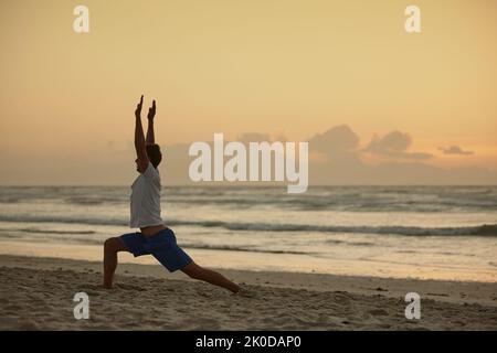 Yoga - the poetry of movement. a man doing yoga on the beach at sunset. Stock Photo