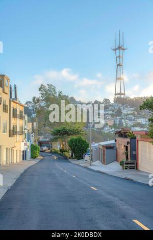 View of Sutro Tower from the road in the middle of residential buildings in San Francisco, CA. There is a view of detached garage on the right against Stock Photo