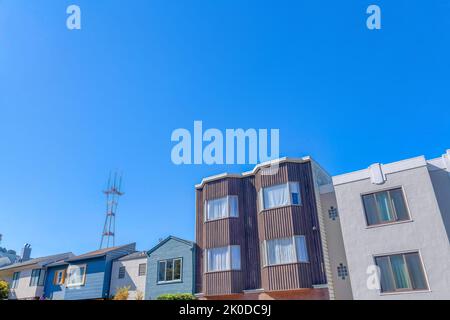 Adjacent suburban houses against the Sutro Tower and clear blue sky background at San Francisco, CA. There is a house on the right with light gray ext Stock Photo