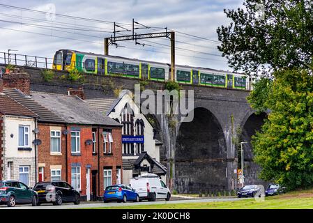 London and North Western railway Class 350 electric multiple unit train heads towards Liverpool passing over houses under bridge arches. Stock Photo