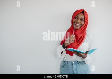Searching for ideas. Thoughtful african american lady in hijab holding notepad and pencil, light background, copy space Stock Photo