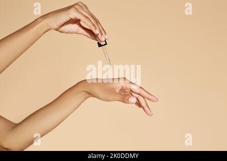 Moisturizing skin of hands with essential oil or serum. Woman applying essential oil to her hands with pipette dropper on beige background Stock Photo