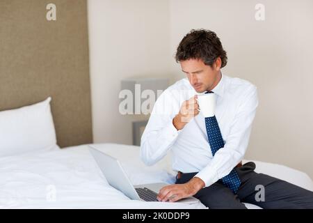 Man holding coffee mug while working on laptop. Confident middle aged business man having a cup of coffee and working on laptop at home. Stock Photo