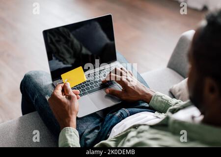Middle aged african american guy typing on computer with blank screen and showing credit card Stock Photo