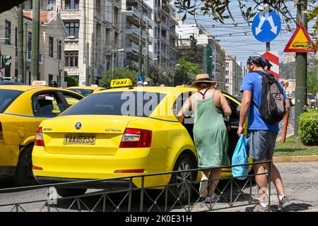 Athens, Greece - May 2022: Two people getting in a yellow taxi on one of the city streets Stock Photo