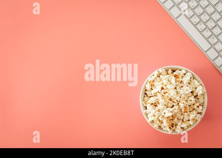 Popcorn and keyboard on pink background, flat lay. Stock Photo