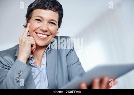 Business woman using digital tablet. Portrait of cheerful mature business woman using tablet PC in office. Stock Photo