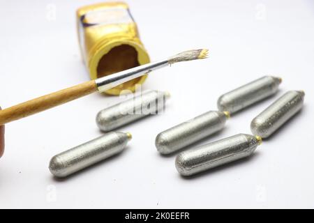Art and crafts work being done using a paint brush and silver color paint on some cylindrical shape object Stock Photo
