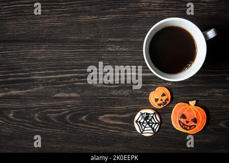 Halloween background, cup of coffee and sweets on wooden table, top view. Orange pumpkin shaped cookies on dark wood planks with space. Party, season, Stock Photo