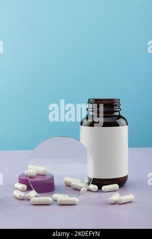 Open bottle for medicines with scattered capsules on a blue background with a blank label. Stock Photo