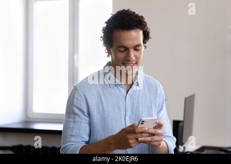 Happy Latin office employee man using online app on smartphone Stock Photo