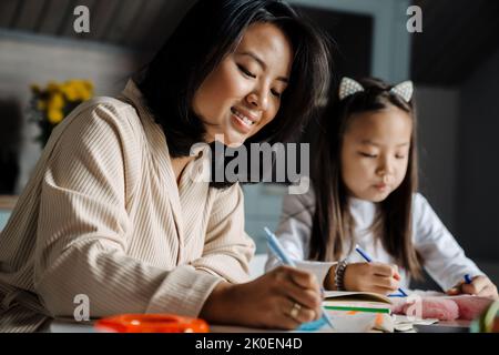 Happy mother smiling while doing homework with her mother at home Stock Photo