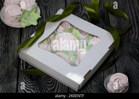Zephyr flowers. Zephyr in a cardboard box. Near samples of marshmallows. Tape for tying the box. On pine boards. Stock Photo