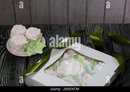 Zephyr flowers. Zephyr in a cardboard box. Near samples of marshmallows. Tape for tying the box. On pine boards. Stock Photo