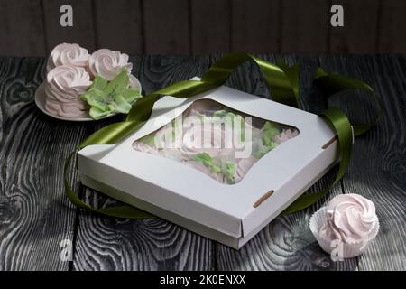 Zephyr flowers. Zephyr in a cardboard box. Near samples of marshmallows. Tape for tying the box. On pine boards. Stock Photo