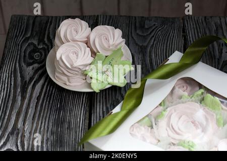 Zephyr flowers. Zephyr in a cardboard box. Near samples of marshmallows. Tape for tying the box. On pine boards. Stock Photo