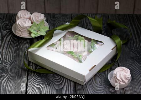 Zephyr flowers. Zephyr in a cardboard box. Near samples of marshmallows. Tape for tying the box. On pine boards. Stock Photo