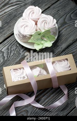 Zephyr flowers. Zephyr in a cardboard box. Near samples of marshmallows. Tape for tying the box. On pine boards. Stock Photo